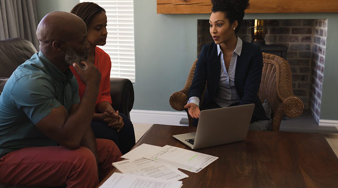 Front view of a female insurance agent and a senior couple discussing over laptop while sitting in the living room at home